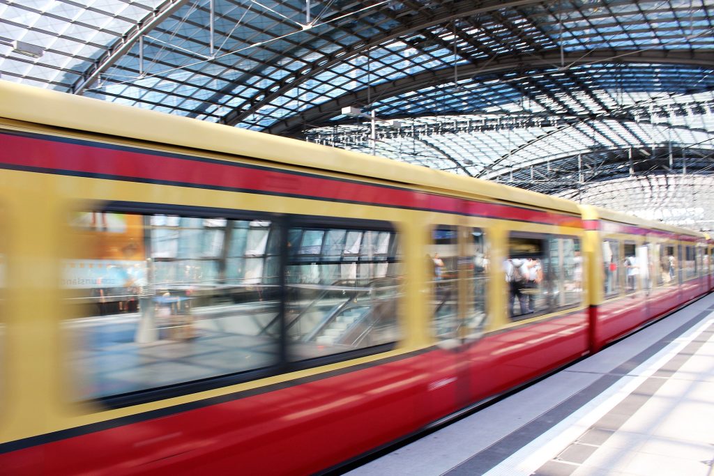 Bahnhof Berlin fährt eine U-Bahn schnell ein. Die Waggons sind rot und gelb. Im Hintergrund ist der Berliner Bahnhof erkennbar.