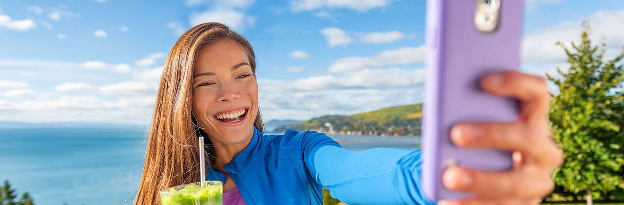 Ein Mädchen mit einem Getränk in der Hand macht mit dem Handy ein Selfie. Foto: Maridav/Adobe Stock.