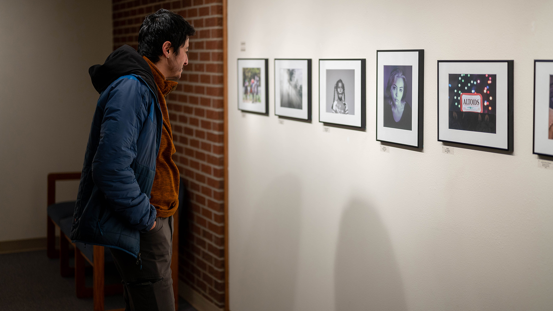 A person standing in a dimly lit gallery looking at photos on a wall