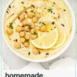 homemade lemon hummus in a white bowl next to a plate of colorful veggies