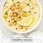 homemade lemon hummus in a white bowl next to a plate of colorful veggies