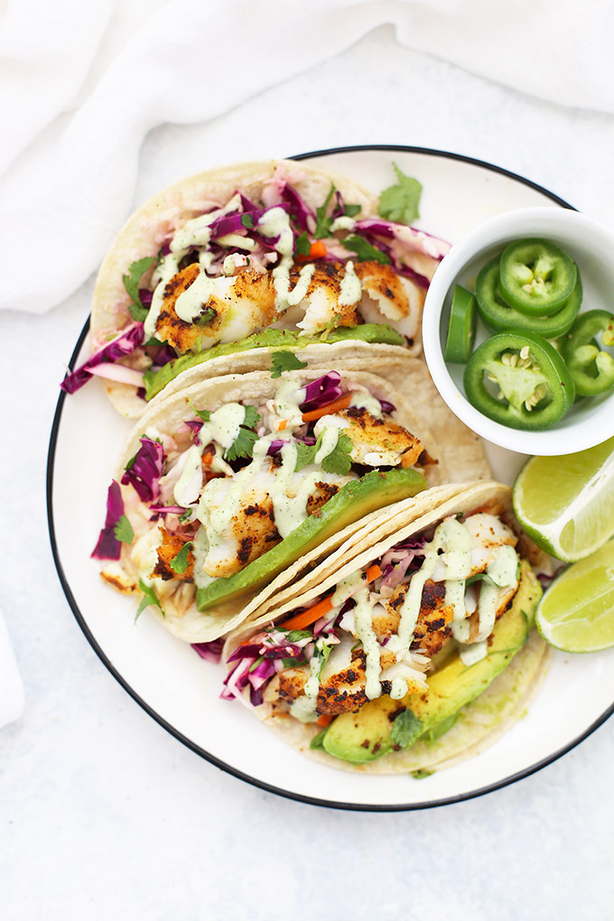 Fish Tacos with Cilantro Slaw and Tomatillo Ranch Dressing. Plated with sliced jalapeños and lime wedges.