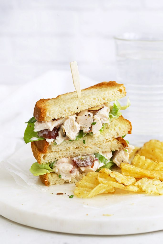 A gluten-free chicken salad sandwich on a marble serving board with kettle chips next to it.