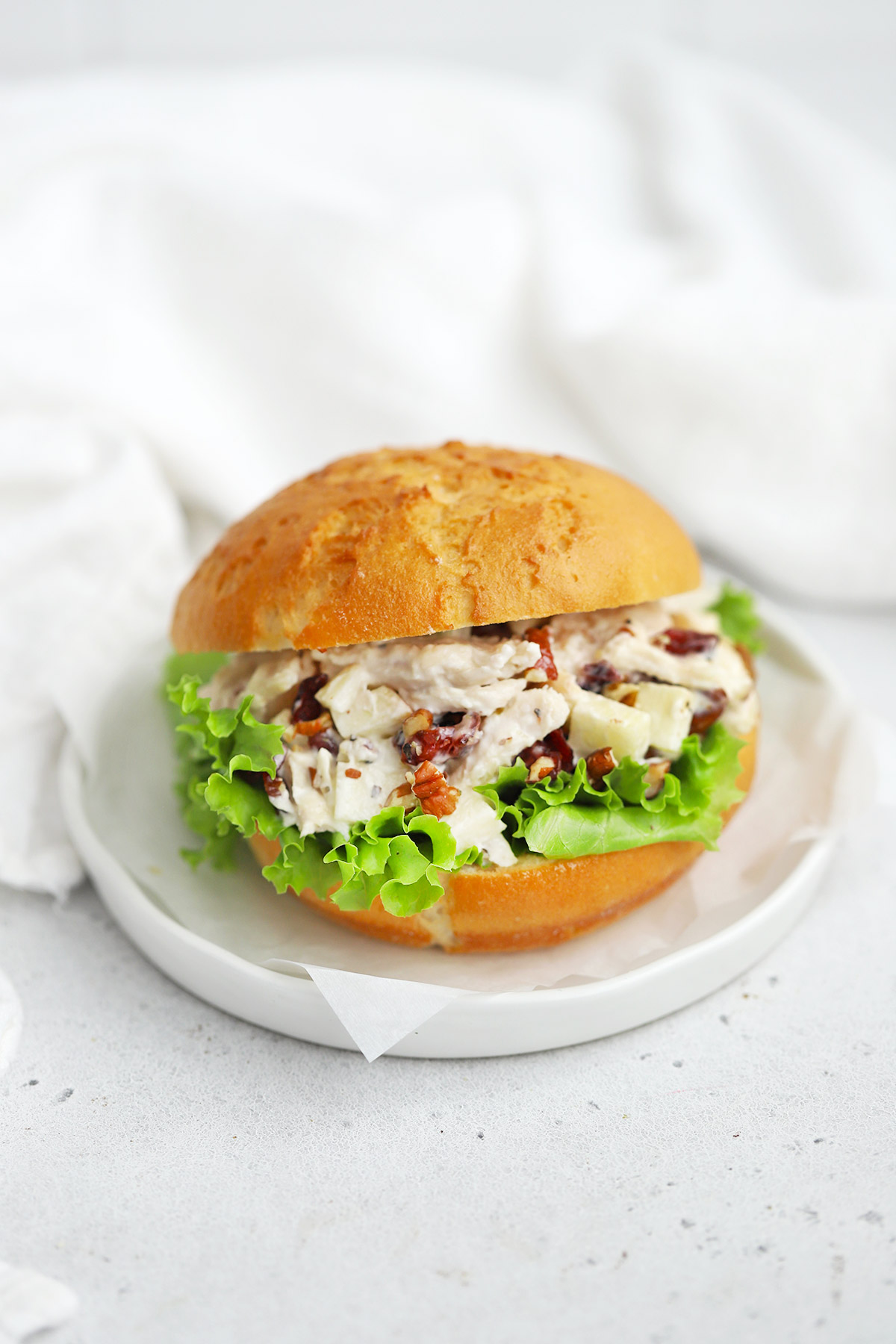 Front view of an apple cranberry chicken salad sandwich made with a gluten-free bun on a white plate. 