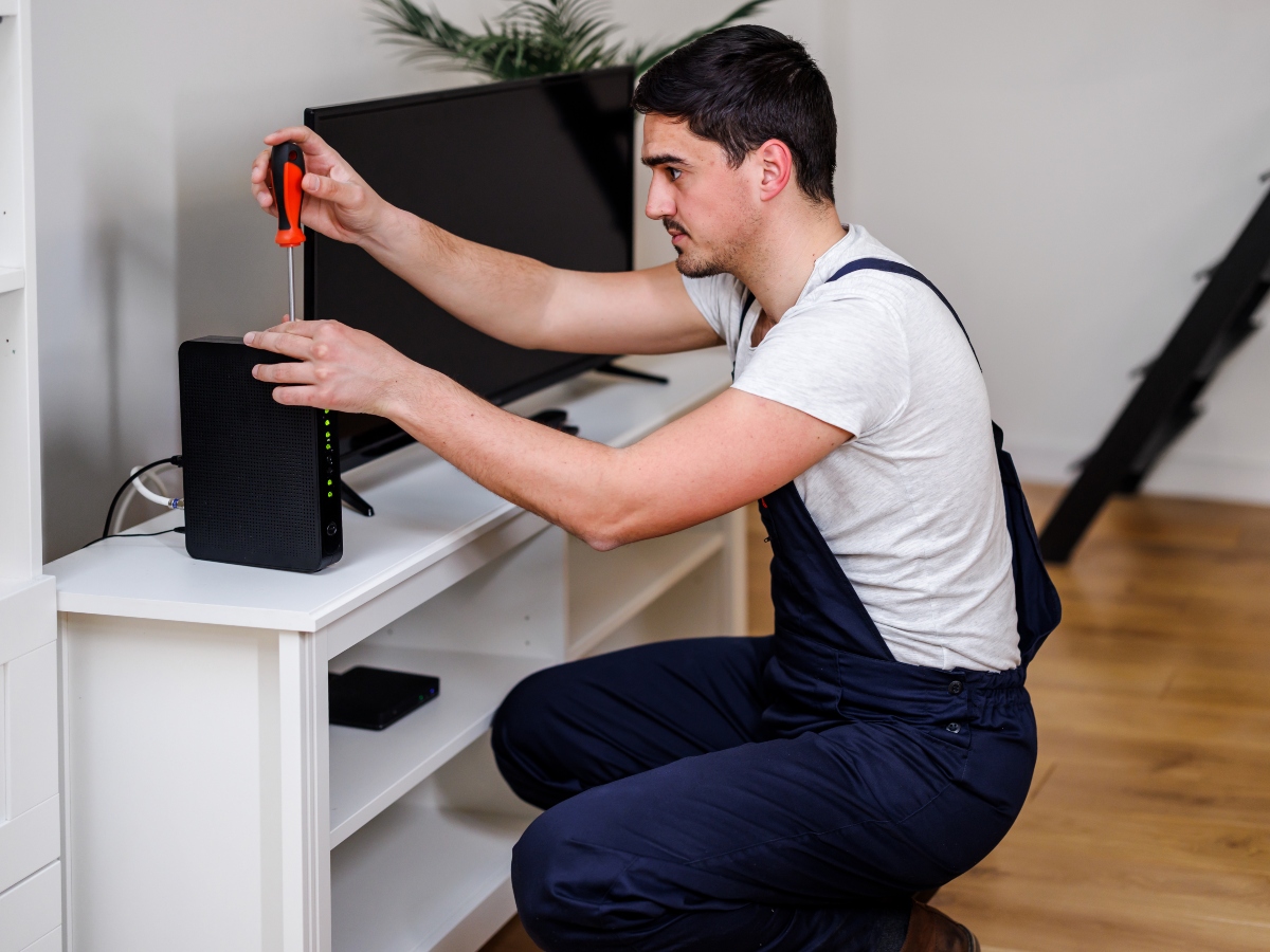 A young electricity worker is repairing a wireless router with a screwdriver.