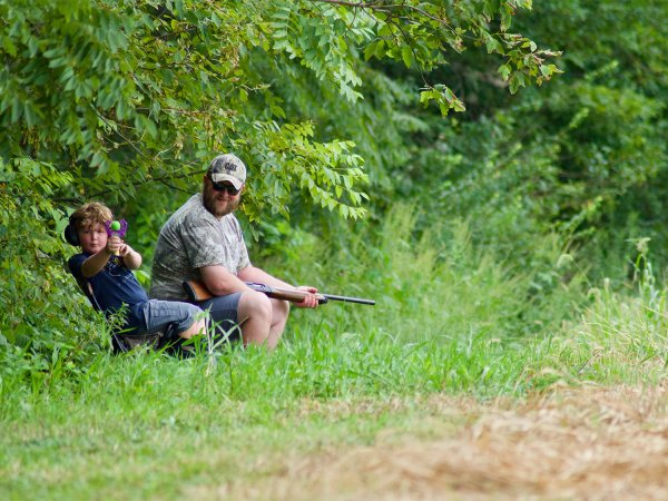 A man and a young boy hunting on the edges of the woods.