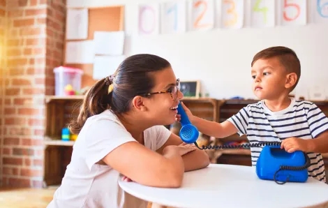 little boy holding a blue phone up to his preschool teacher's ear