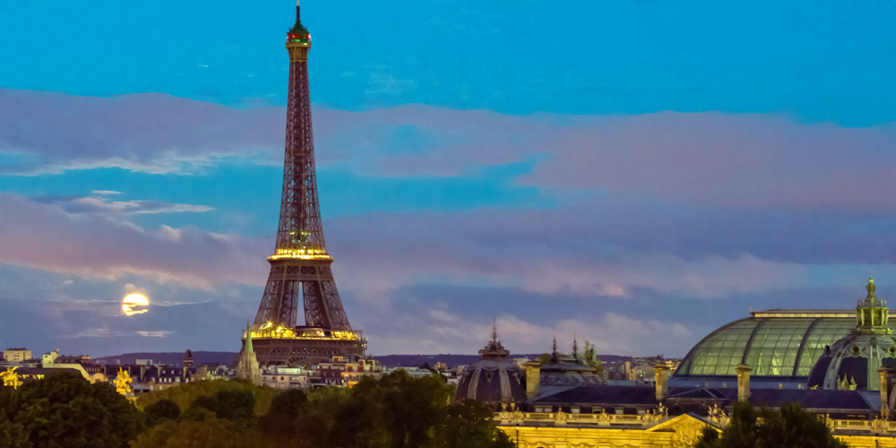 A nightview of the Eiffel Tower, shot from the rooftops of Paris, with the full moon in the background