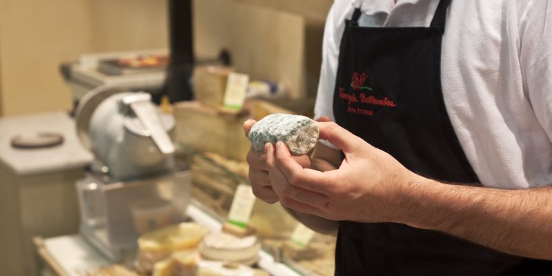 A cheese monger holds a log of cheese during a Paris Cheese & Wine Tasting