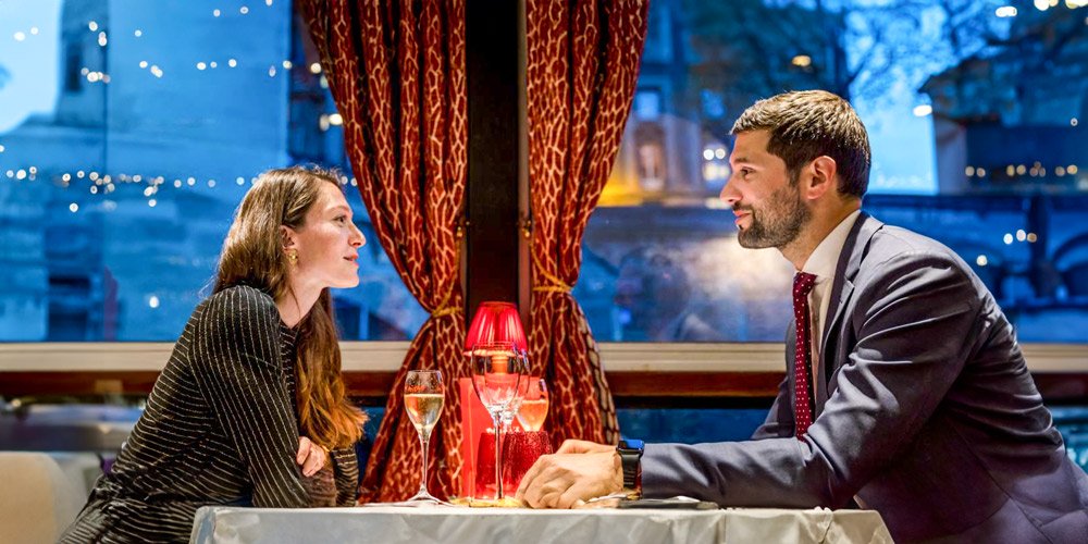 A couple at a table during a dinner cruise by Maxim's of Paris