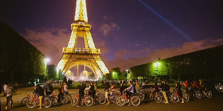 Cyclists pose in front of the Eiffel Tower during a Paris Night Bike Tour