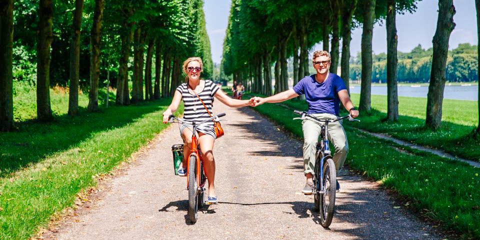 A couple holding hands while cycling on a path though the gardens of Versailles on a Bike Tour with Skip-the-Line Entrance