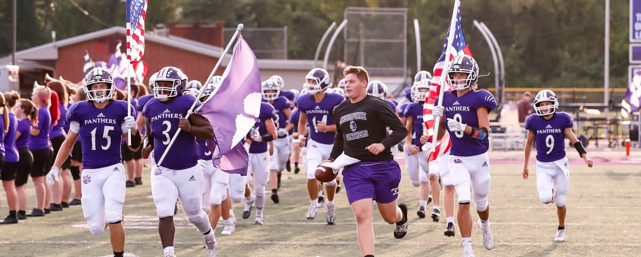 Football team running onto field with flags and banners wearing purple