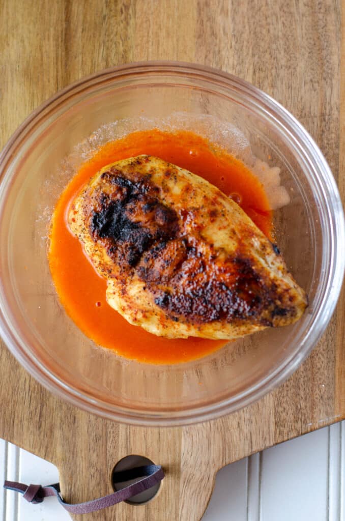 grilled chicken breast in a bowl of buffalo sauce.