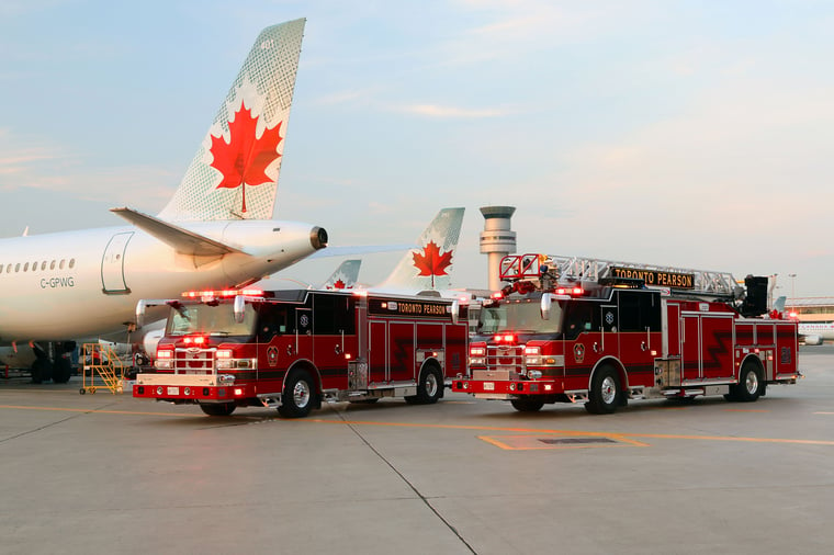 Two Pierce PUC firetrucks parked outside on a cloudy day near an airplane. 