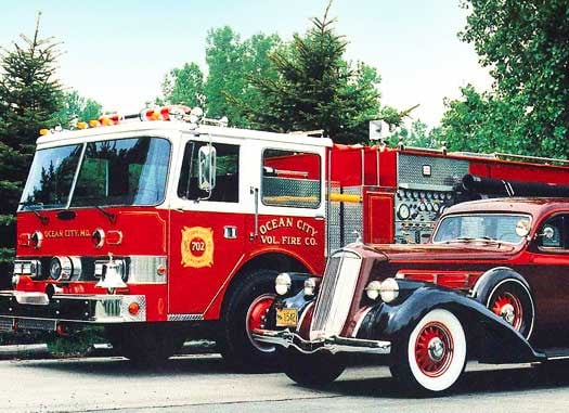 Pierce Manufacturing Arrow fire apparatus parked outside beside a vehicle surrounded by trees.