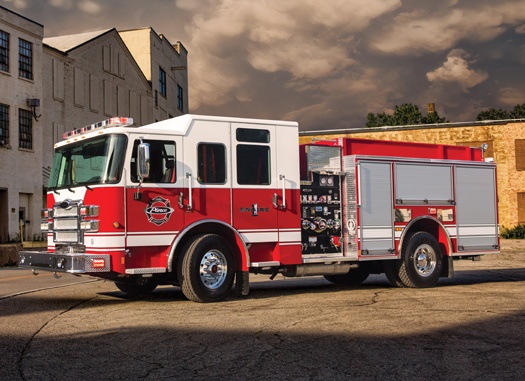 A Pierce Manufacturing firetruck parked outside near a building on a cloudy day. 