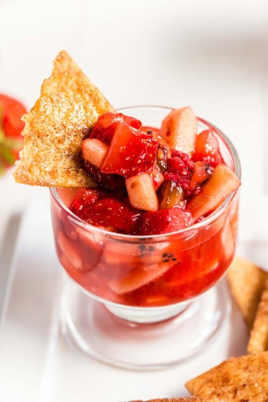 A small glass cup of fruit salsa with a cinnamon chip stuck in it