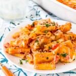 Plate full of baked ziti with a pan of baked ziti in the background