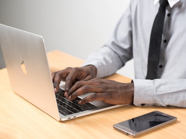 A person using a Macbook laptop on a wooden table with an iPhone next to them.