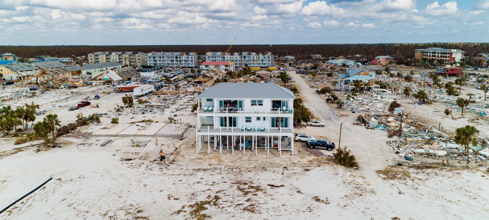 White house standing alone among destroyed houses on a beach.