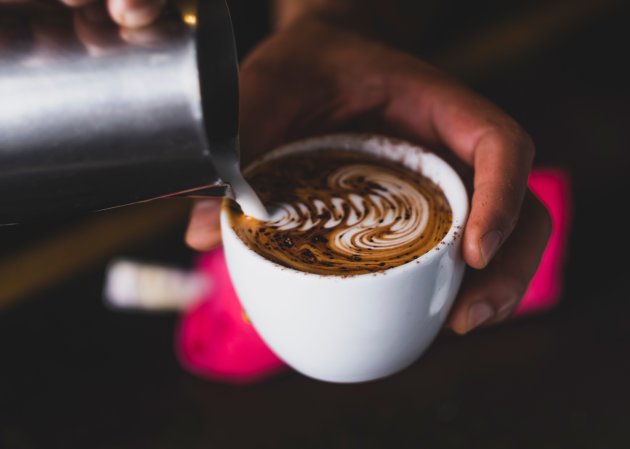 A person pouring frothed milk into a coffee cup