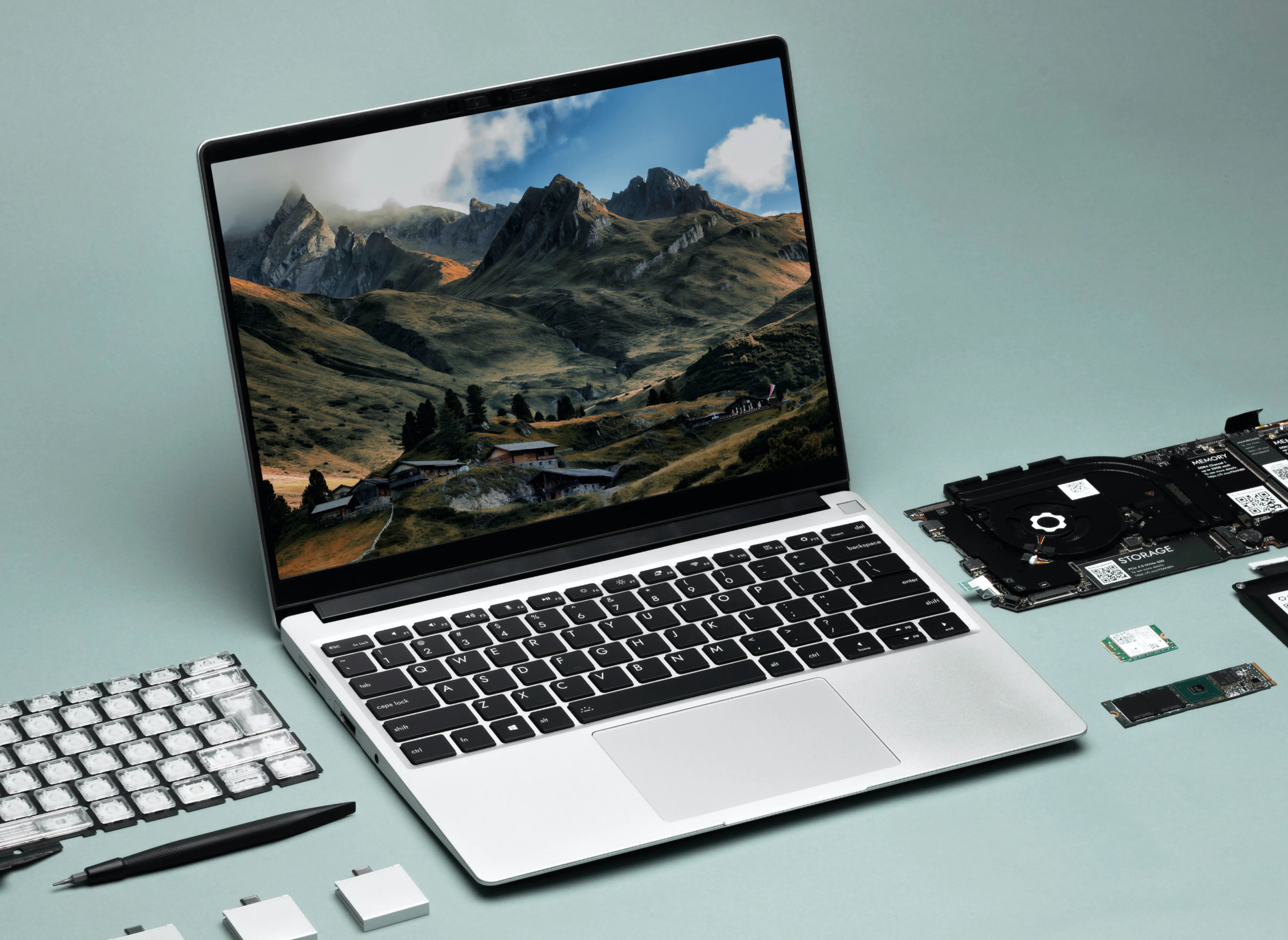 A framework modular laptop on a blue background surrounded by extra parts including a main board and a keyboard.