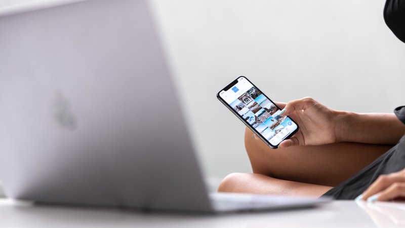 A person using an iPhone in front of a silver Macbook laptop.