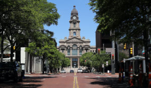 A few vehicles are seen parked along or navigating Main Street during the noon hour by the Tarrant County Court House in downtown Forth Worth, Texas, Wednesday, March 25, 2020. (AP Photo/Tony Gutierrez)