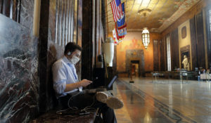 A reporter wearing a mask sits alone as he works outside the Louisiana state senate chamber in Baton Rouge, Louisiana. (AP Photo/Gerald Herbert)