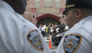 Mourners arrive as NYPD officers stand guard at the funeral service of Eric Garner, the 43-year-old New York City man whose death while in police custody led to accusations of police misconduct. The city of New York City settled out of court and paid the Garner family $5.9 million over the case. (AP Photo/John Minchillo)