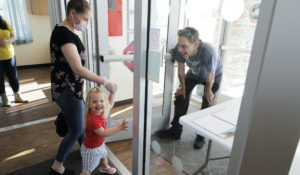 Samantha Sulik, left, director of the Frederickson KinderCare daycare center, in Tacoma, Wash., looks on as Michael Canfield, right, waits in an entryway to pick up his daughter Aurora at the end of the day.  (AP Photo/Ted S. Warren)