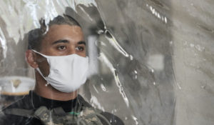 A cadet candidate stands behind a plastic screen as he gets instructions on his arrival at the U.S. Military Academy in West Point, N.Y. Candidates are COVID-19 tested immediately upon arrival, wear masks, and practice social distancing. (AP Photo/Mark Lennihan)