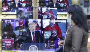 A woman wearing a face mask walks by the window of a shop with TV screens showing an image of U.S. President Donald Trump during a news program, in Milan, Friday, Oct. 2, 2020. Trump said early Friday that he and first lady Melania Trump have tested positive for the coronavirus, a stunning announcement that plunges the country deeper into uncertainty just a month before the presidential election. (AP Photo/Luca Bruno)