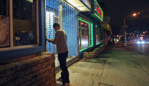 On a mostly empty street, an employee of Justin's BBQ closes up for the night in an area where coronavirus cases have recently spiked in Newark, N.J., Thursday, Nov. 12, 2020. Residents in some parts of New Jersey's largest city are facing a 9 p.m. curfew for at least the rest of the month as officials seek to stop a surge in coronavirus infections. (AP Photo/Seth Wenig)