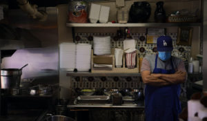 Valo Martinez, a 63-year-old cook working at El Rancho Grande, waits for customers on Olvera Street in downtown Los Angeles, Wednesday, Dec. 16, 2020. The tree-covered brick alley typically teeming with tourists is empty. Many of the shops that sell everything from traditional Mexican folk dresses to paintings of artist Frida Kahlo to sombreros are padlocked and the ones open have few, if any, customers. (AP Photo/Jae C. Hong)