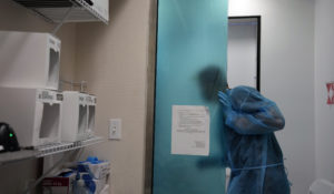 Jainer Munoz, a Venezuelan doctor working as a nurse as he studies for his U.S. medical license, leans out the door to talk to a passenger awaiting his test results, as he runs rapid PCR and antigen tests on nasal swabs at a testing center operated by Nomi Health inside Miami International Airport, Friday, Dec. 17, 2021, in Miami. (AP Photo/Rebecca Blackwell)