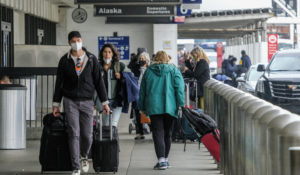 Travelers wearing face masks arrive at the Los Angeles International Airport in Los Angeles, Wednesday, Dec. 22, 2021.  AP Photo/Ringo H.W. Chiu)