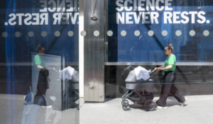 A woman pushes a baby in a stroller past a sign hanging outside Pfizer headquarters in New York, Monday, May 23, 2022. (AP Photo/Mary Altaffer)