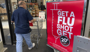 In this Wednesday, Oct. 6, 2021, photograph, a shopper passes a sign urging people to get a flu shot outside a Hy-Vee grocery store in Sioux City, Iowa. (AP Photo/David Zalubowski)