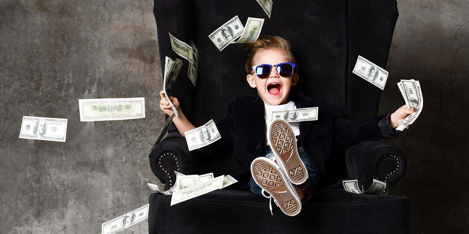 Boy sitting with his feet up on a desk, wearing sunglasses and throwing money in the air.