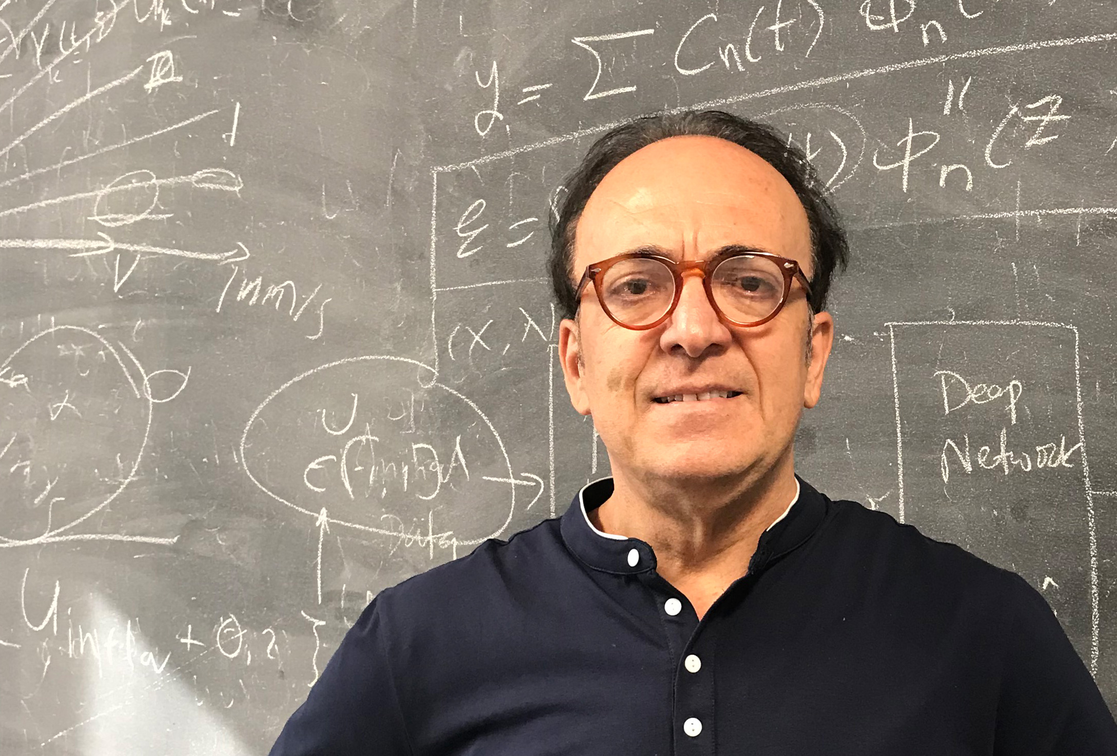 George Karniadakis in a black shirt, standing in front of a chalkboard.