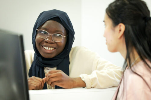 Two undergraduate students are seated at a desk, collaborating on a computing task. 