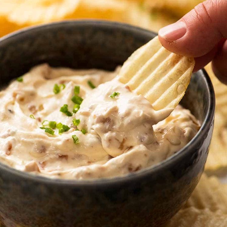 Hand dipping crinkle cut potato chips in creamy homemade French Onion Dip