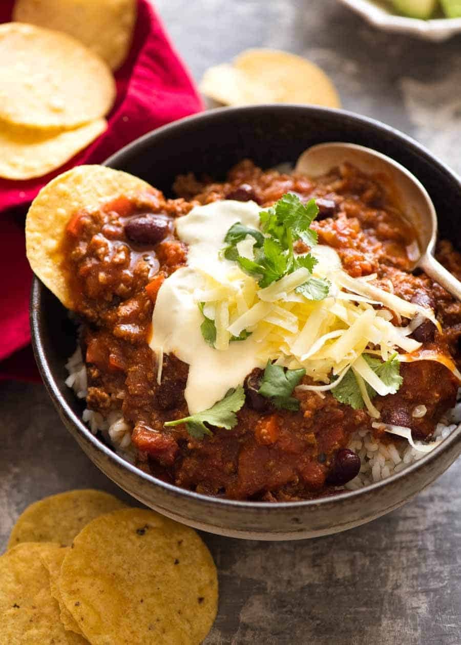 Chili Con Carne served over rice with sour cream, grated cheese and coriander toppings, ready to be eaten