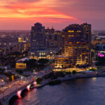 Aerial establishing shot of West Palm Beach, Florida at dusk on a spring evening, looking across Lake Worth Lagoon and Royal Park Bridge towards hotels and condo towers