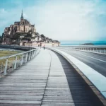 View of Mont-Saint Michel from a distance with walkway in centre image. Just one of many amazing cities to explore in Normandy