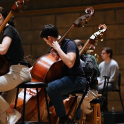 A group of University of Rochester students performing together on cellos during a concert.