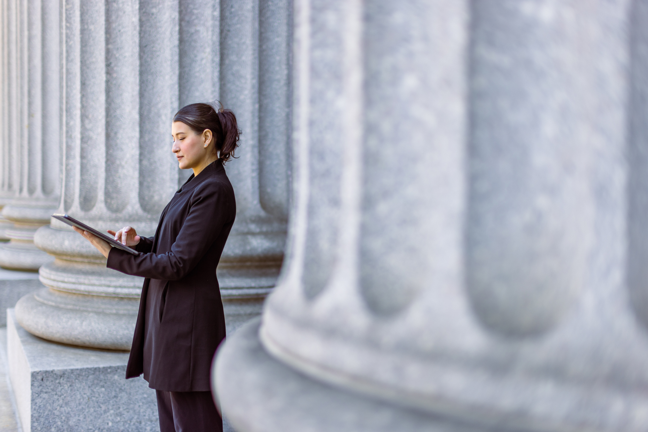 A woman in a suit in front of a government building, referencing her notepad