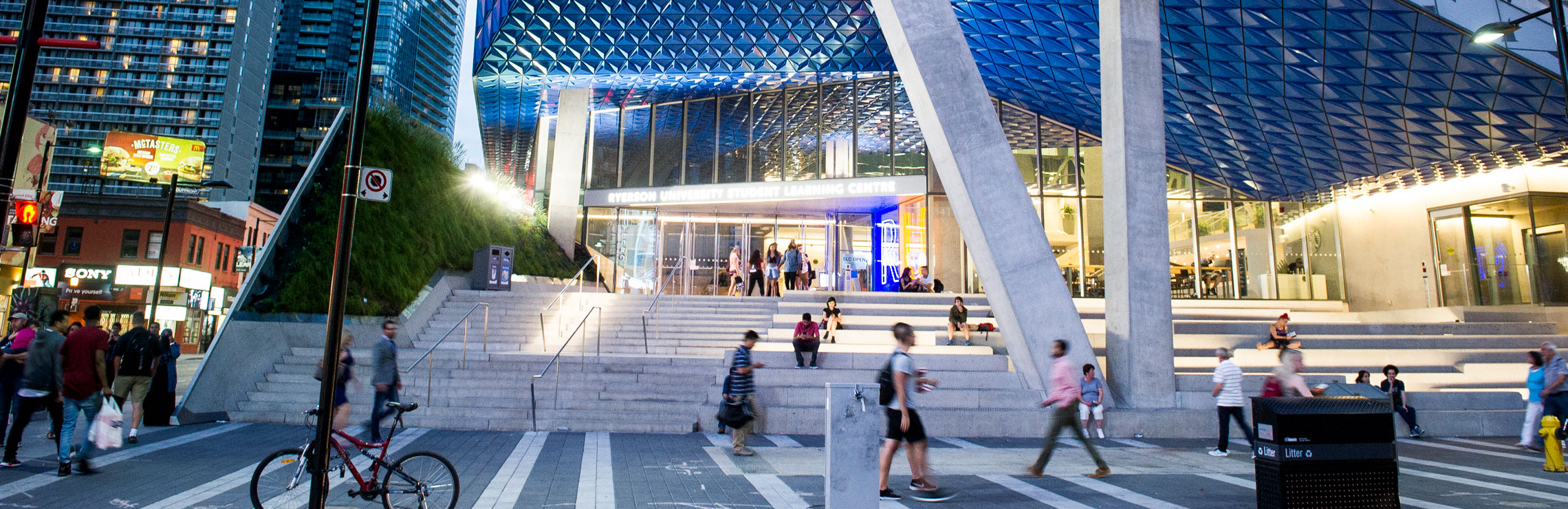 Pedestrians walking along Gould St. passing the front entrance of Ryersonâs Student Learning Centre. 